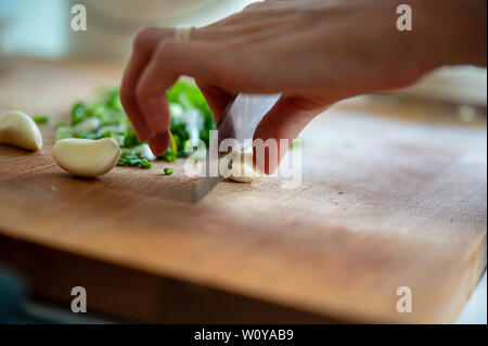 Closeup view of female hand cutting garlic clove on a wooden board with a sharp knife. Stock Photo