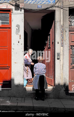 Two older women wearing aprons standing in street on doorstep have a conversation chatting talking Porto Oporto Portugal Europe  KATHY DEWITT Stock Photo