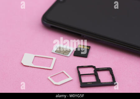 A black smartphone next to the microSD memory cards and the SIM card on a pink background Stock Photo