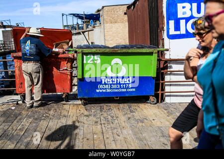 Puerto Peñasco, Sonora, October 20, 2017.- Two American women tourists stroll the tourist dock of Puerto Peñasco while a May adult man of extreme poverty looks for food inside the trash contents. Dos mujeres turistas norteamericanas pasean por el muelle turístico de Puerto Peñasco mientras un hombre adulto mayo de pobreza extrema  busca comida dentro de los contenidos de basura. (Foto: Luis Gutierrez /NortePhoto.com) Stock Photo