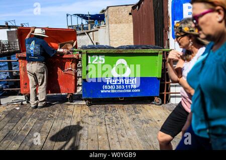 Puerto Peñasco, Sonora, October 20, 2017.- Two American women tourists stroll the tourist dock of Puerto Peñasco while a May adult man of extreme poverty looks for food inside the trash contents. Dos mujeres turistas norteamericanas pasean por el muelle turístico de Puerto Peñasco mientras un hombre adulto mayo de pobreza extrema  busca comida dentro de los contenidos de basura. (Foto: Luis Gutierrez /NortePhoto.com) Stock Photo