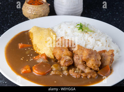 Rice with Japanese curry with omelette and chicken fried topping in white plate. Stock Photo