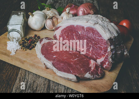Raw beef cutting for steak with seasoning ingredient on wooden plate with grey and dark low lighting. Stock Photo