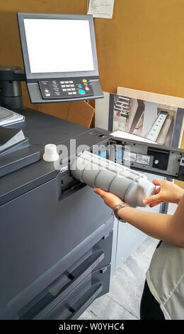Close-up of young woman working at color printer inserting print toner. Stock Photo