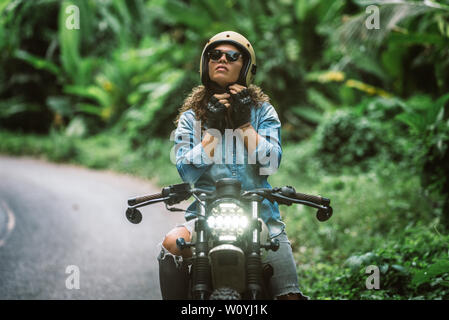 Beautiful female biker driving a cafe' racer motorbike - Pretty girl driving a motorbike and enjoying the roadtrip