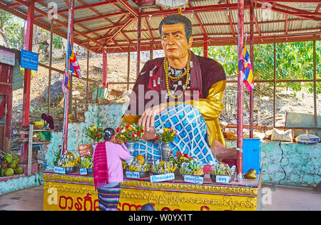 POPA, MYANMAR - FEBRUARY 26, 2018: The Buddhist devotee is making donation at the altar of Nat (Spirit deity) in covered outdoor shrine, located on th Stock Photo