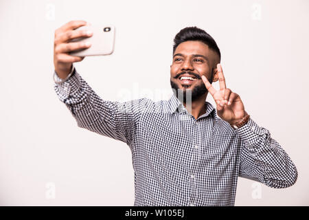 Indian young man with beard and mustache taking selfie using smartphone, isolated over white background Stock Photo