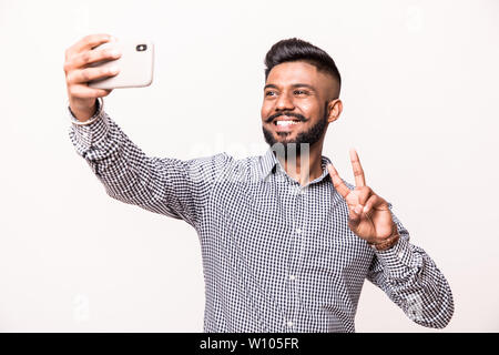 Indian young man with beard and mustache taking selfie using smartphone, isolated over white background Stock Photo