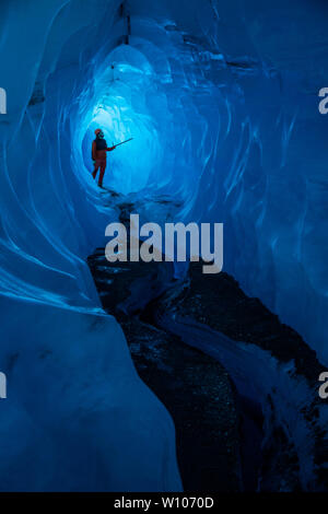 Ice climbing guide deep inside an ice cave on a glacier in Alaska admires a narrow band of thin ice where light shines through Stock Photo