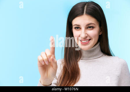 beautiful young caucasian woman pressing a virtual button, looking at camera smiling, isolated on blue background Stock Photo