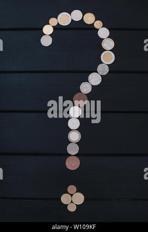 Scattered coins of different countries in the form of a question mark and an exclamation point on wooden table. Stock Photo