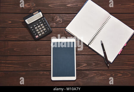 Top view of tablet, smartphone, calculator, notepad on wooden background, planning personal income, financial concept. typing on the calculator for mo Stock Photo