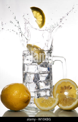 Lemons falling into a glass of ice water with splashes against isolated on white background. Refreshing Beverage Stock Photo