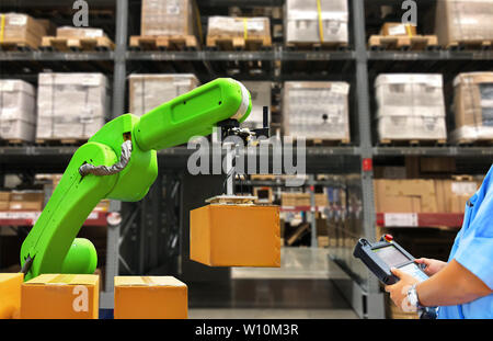Industrial robot holding a box and worker operating a robot machine with a control panel on stock shelves background Stock Photo