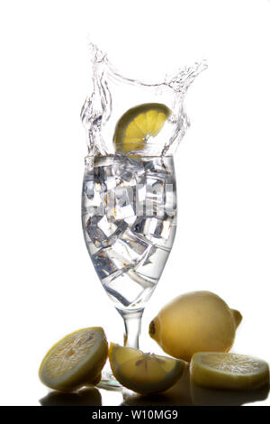 Lemons falling into a glass of ice water with splashes against isolated on white background. Refreshing Beverage Stock Photo