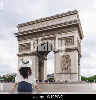 Young traveler woman in white hat looking at Arc de Triomphe, famous landmark and travel destination in Paris, France in summer Stock Photo