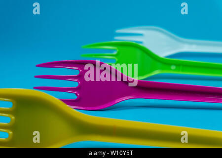 Yellow purple green and white cutlery plastic forks arranged on blue background. Color trends and recycling, plastic waste problem concepts Stock Photo