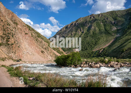 River flowing between green hills with snow-capped mountain peaks on the horizon against a cloudy sky. Stock Photo