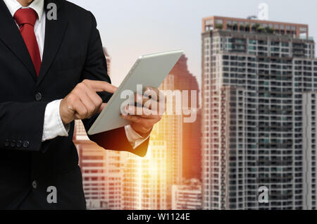young handsome business man in suit reading information about finance news with mobile tablet with during sunrise and cityscape background Stock Photo