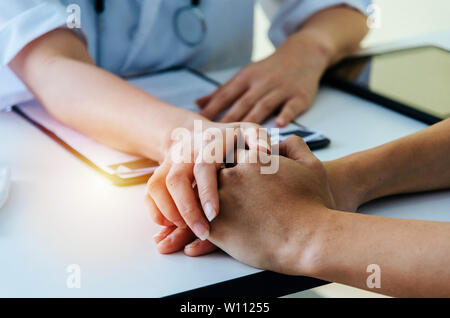 friendly female doctor with stethoscope support and holding patient hand with clipboard on desk in hospital or clinic, encouragement, health care Stock Photo