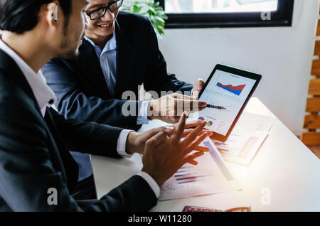 young partner business man investor talking about financial statistics chart information in mobile tablet together sitting in meeting room at office Stock Photo