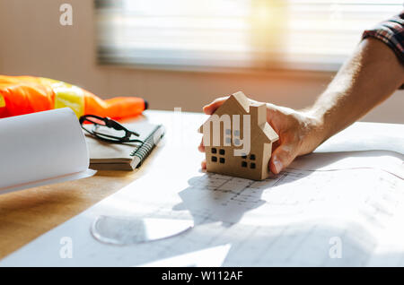professional architect, engineer or interior hand with house model and blueprint on workplace desk in office center at construction site, contractor Stock Photo