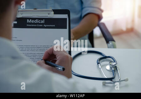 back view of young male doctor or pharmacist writing prescription on clipboard with stethoscope on desk and patient sitting in hospital, health care Stock Photo