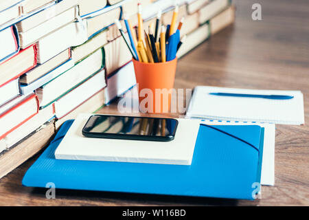Stack of books, hardback books, smartphone, plastic folder, notebook and pencils on wooden table copy space for text Stock Photo