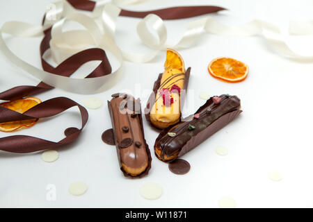 A close-up of a set of three eclairs with different fillings and design isolate on a white surface decorated with chocolate drops, dried oranges and b Stock Photo