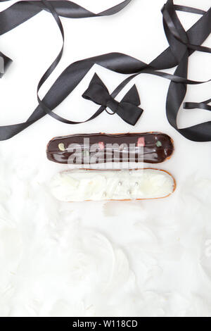 Set of two eclairs with a decor of black and white chocolate isolate on a white surface decorated with white feathers and brown ribbons, copyspace Stock Photo