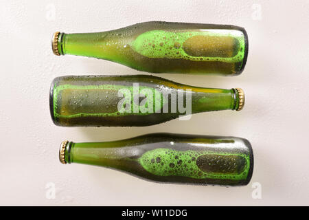 Three green bottles with alcoholic beverage on white table. Horizontal composition. Top view. Stock Photo