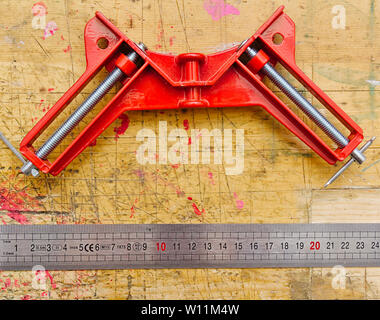 Angle clamp and ruler on red paint stained wooden workbench surface background. Stock Photo