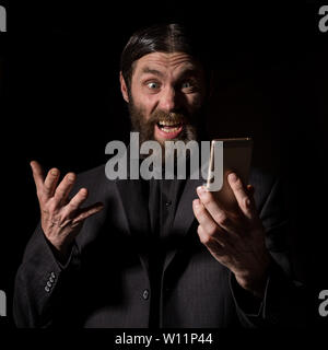 Old believer senior priest with a smartphone, bearded old man is calling on a dark background. Stock Photo