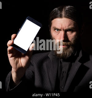 Old believer senior priest with a smartphone, bearded old man is calling on a dark background. Stock Photo