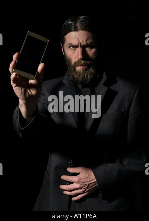 Old believer senior priest with a smartphone, bearded old man is calling on a dark background. Stock Photo