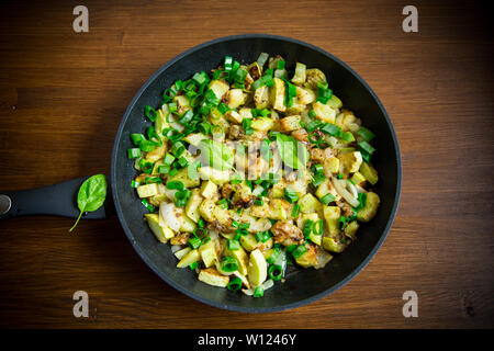 green zucchini fried with onions and herbs in a pan on a wooden table Stock Photo