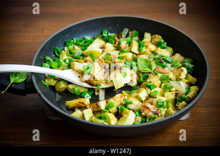 green zucchini fried with onions and herbs in a pan on a wooden table Stock Photo