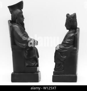 Two black miniature Chinese chess figurines seated face to face on a grey studio background, black and white still life. Stock Photo