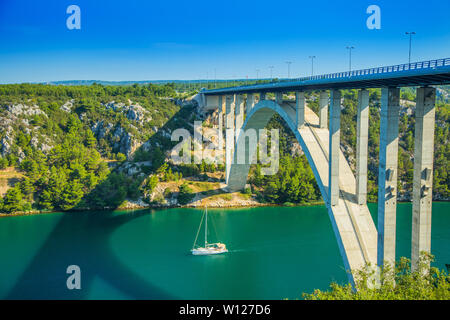 Aerial panorama view of bridge on highway over Krka river in deep canyon in Croatia and sailing boat passing under. Beautiful landscape. Stock Photo
