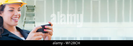 Female Contractor Wearing Hard Hat Using Cell Phone Against Dywall Banner Background with Ladder. Stock Photo
