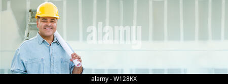 Hispanic Male Contractor Wearing Hard Hat Against Drywall Banner Background with Ladder. Stock Photo