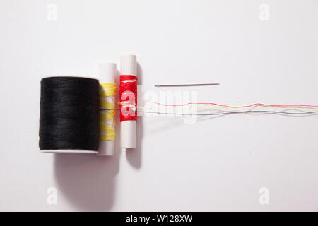 Various sizes and colours of thread and a needle spread long against a white backdrop Stock Photo