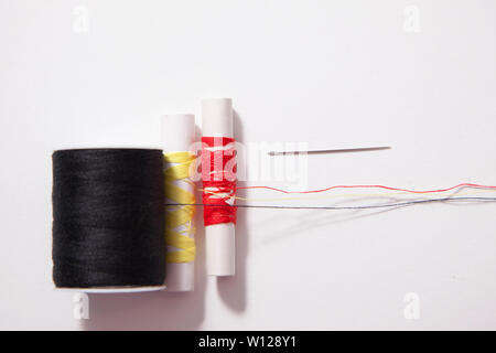 Black, yellow and red thread and needle on white background Stock Photo
