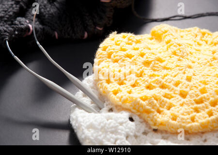 Yellow and white knitted hats with grey blanket and needles Stock Photo