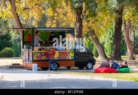 Skopje, Macedonia..  Locals buying and drinking coffee from food colorful truck in park on a sunny fall day Stock Photo