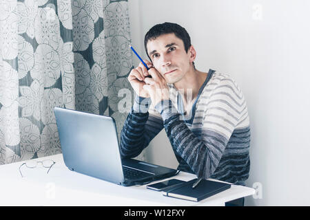 Portrait of young man In casual wear on the job working on laptop looking at with thoughtful face Stock Photo