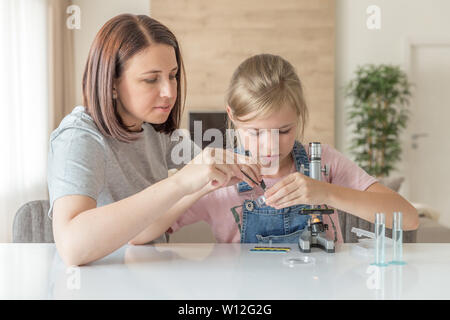 Mother and daughter make chemical experiments with microscope at home Stock Photo