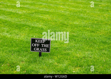 Sign saying keep off the grass in white on black on a beautifully mowed English lawn with diagonal stripes Stock Photo