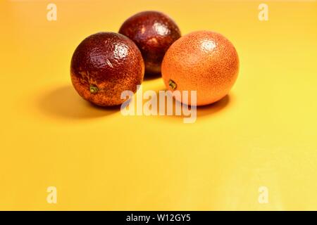 3 red oranges in the center from above on a yellow substrate. Located close to each other. Glossy shiny skin. Stock Photo