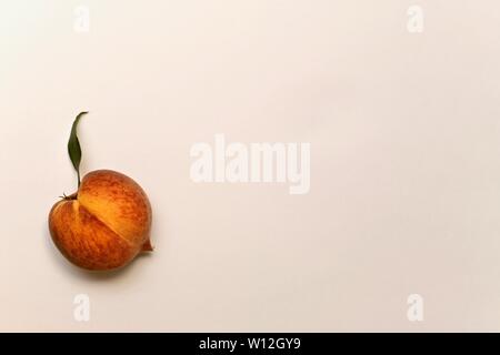Ripe yellow-red peach with green leaf up. With a light shadow bottom. On a light background below left. Stock Photo